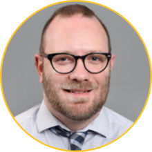 Man with short, light-brown hair and a beard wearing glasses and a tie