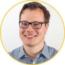 Man with short brown hair and glasses wearing a plaid button up shirt
